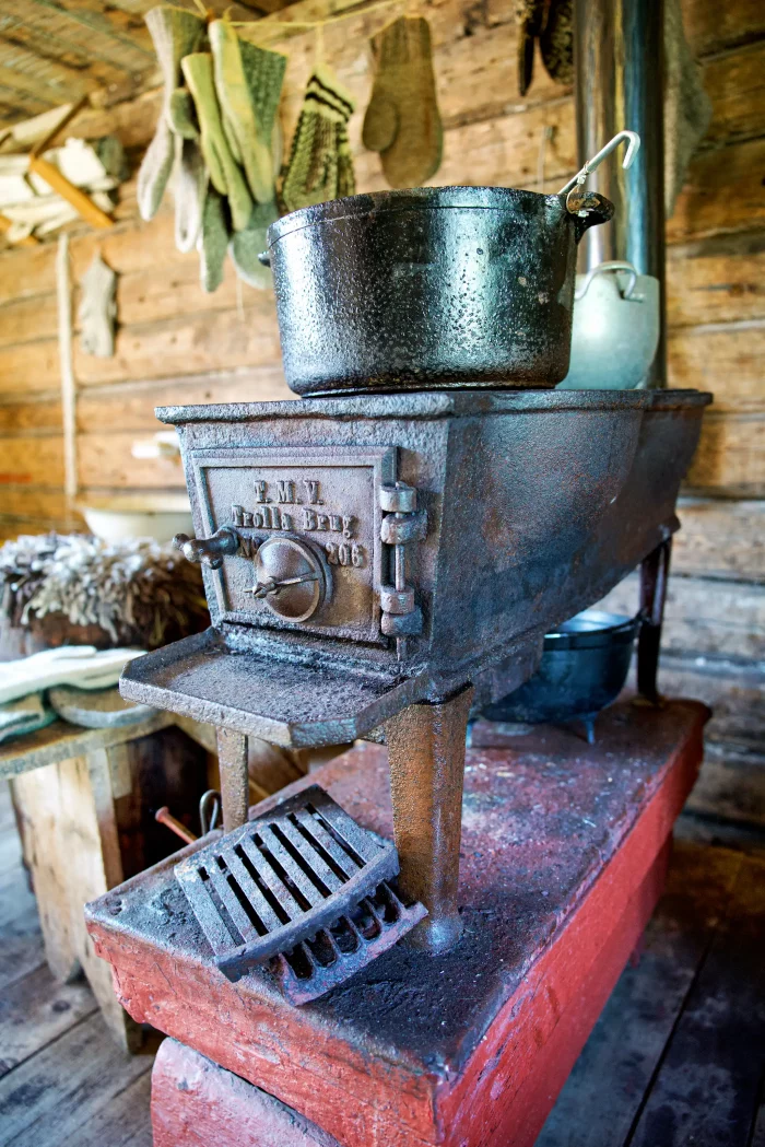 Alter gusseiserner Holzofen mit Topf und Kelle in einer rustikalen Holzhütte