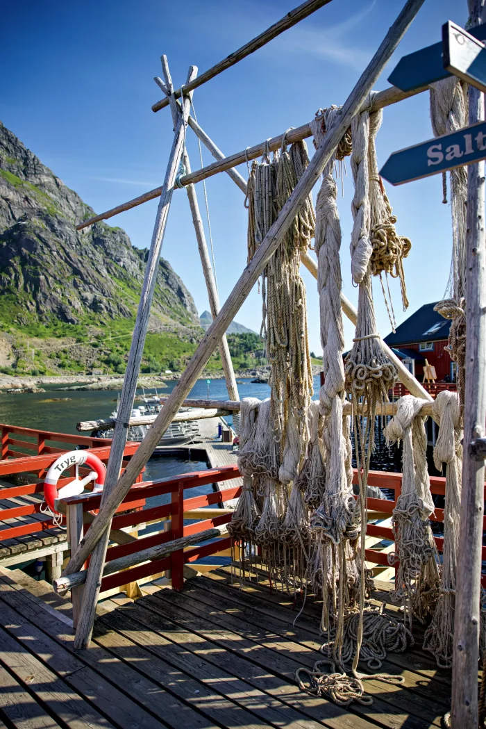 Getrocknete Fischernetze hängen an einem Holzgestell auf einem Pier mit Blick auf Fjord und Berge im Hintergrund
