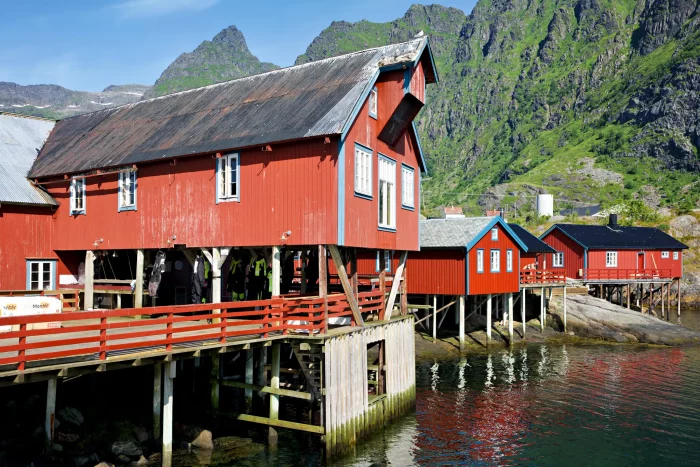 Rote Holzhäuser auf Stelzen am Wasser vor grünen Bergen in Norwegen