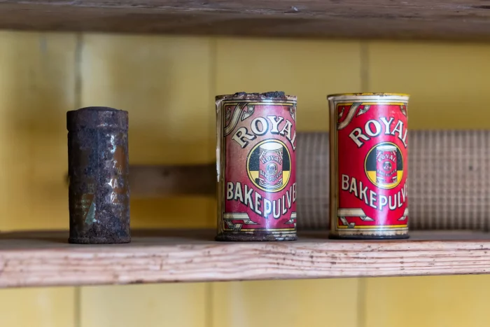 Drei alte Backpulverdosen, zwei davon mit der Marke Royal, auf einem Holzregal