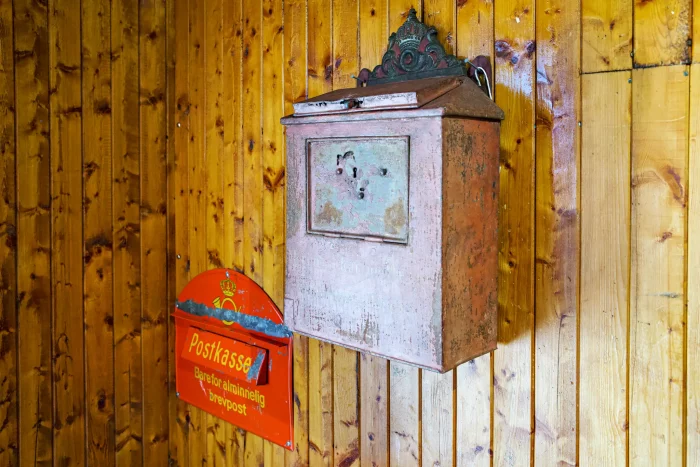 Alte, rostige Metallpostkasten an einer Holzvertäfelung mit rotem Schild 'Postkasse' darunter