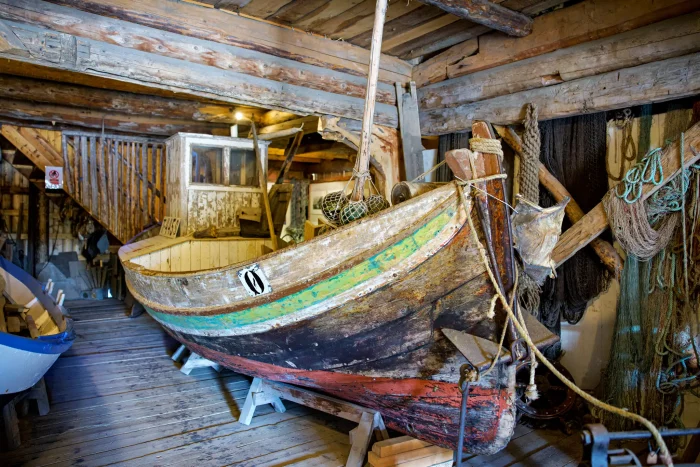 Altes Holzboot mit abgenutztem Anstrich in einer rustikalen Bootshalle mit Holzplanken und Seilen