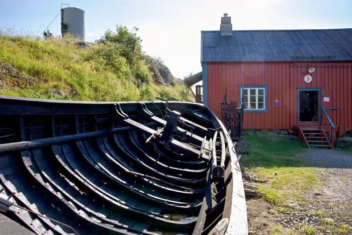 Schwarzes Holzboot vor rotem Holzhaus mit Treppe und Fenster in sonniger Landschaft