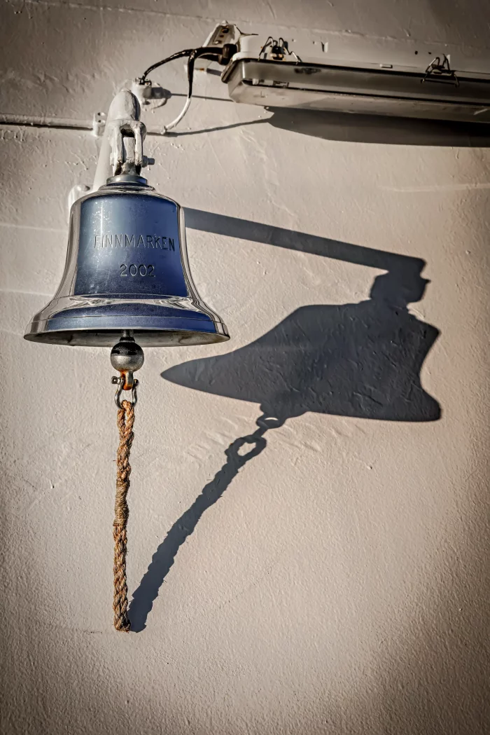 Schiffs-Glocke mit der Gravur 'FINNMARKEN 2009' an einer Wand montiert, mit Schatten an der Wand