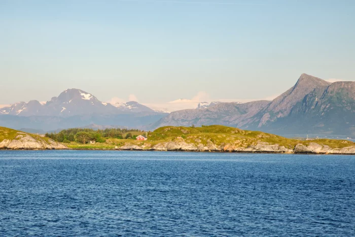 Blick auf eine norwegische Küstenlandschaft mit Bergen im Hintergrund und ruhigem Meer im Vordergrund