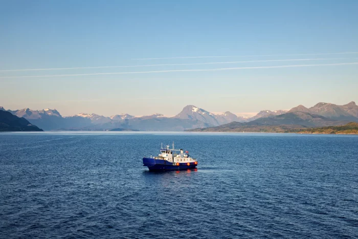 Kleine Fähre auf ruhigem Meer vor Bergkulisse mit klarem Himmel
