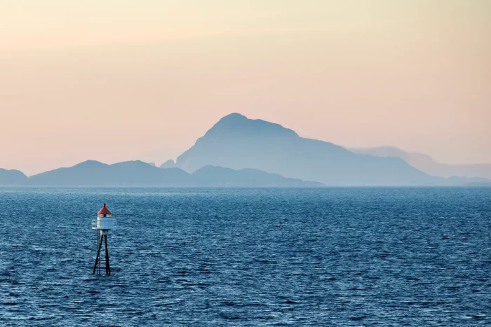 Leuchtturm auf Stelzen im Meer vor einer Bergkette bei Sonnenaufgang oder Sonnenuntergang