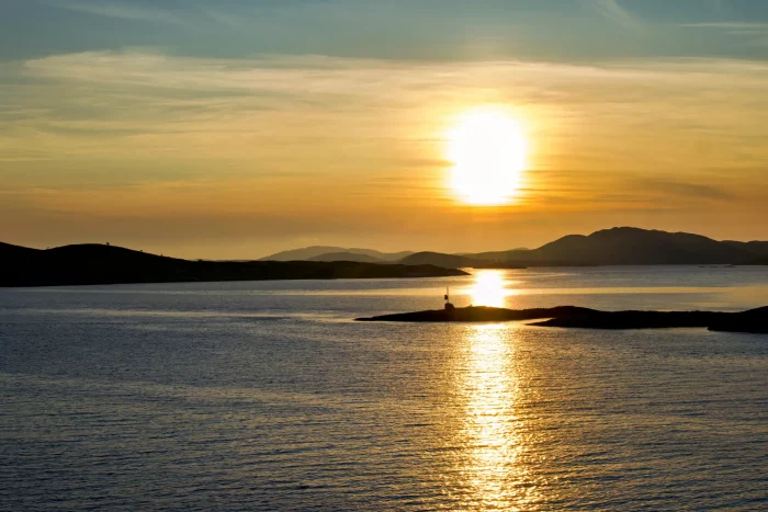 Sonnenuntergang über ruhiger See mit kleinen Inseln und Bergen im Hintergrund
