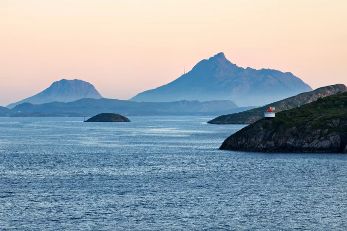 Fjord mit ruhigem Wasser, kleinen Inseln und Bergen im Hintergrund bei Sonnenuntergang