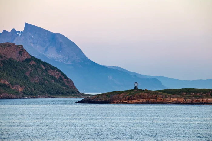 Kleiner Felsen mit Polarkreis-Denkmal vor Fjord und Bergen im Dämmerlicht