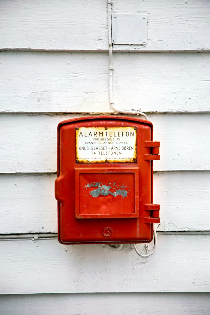 Rotes Alarmtelefon an weißer Wand mit norwegischer Beschriftung für Notfälle
