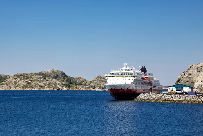 Passagierschiff Hurtigruten liegt am Kai in einer felsigen Küstenlandschaft unter klarem Himmel
