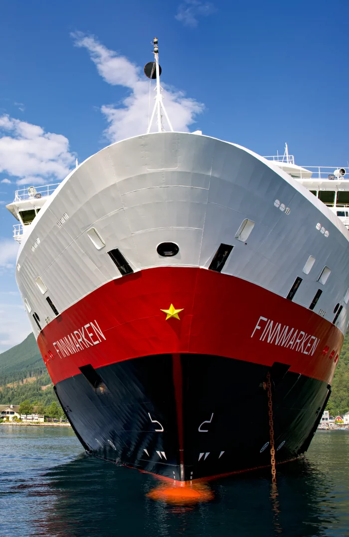 Bug des Hurtigruten-Schiffs Finnmarken mit rotem Rumpf und gelbem Stern, im Hafen bei klarem Himmel