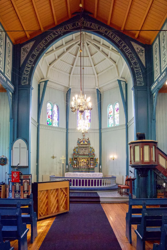 Innenraum einer Kirche mit Altar, Kronleuchter, bunten Glasfenstern und hölzernen Bänken