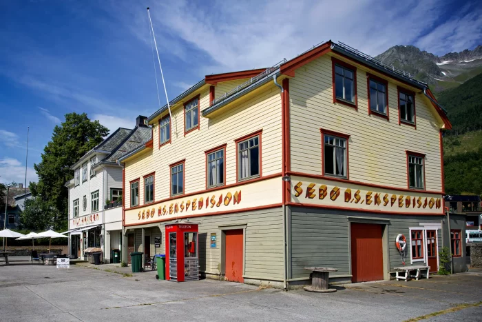 Gelbes, zweistöckiges Gebäude mit rotem Dach und Schriftzug 'Sebo AS Ekspedisjon' an der Fassade in einem norwegischen Hafenort