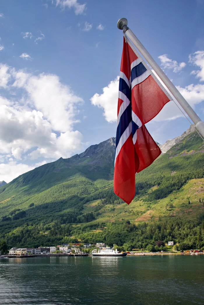 Norwegische Flagge vor Fjord mit Bergen und Hurtigruten-Schiff im Hafen