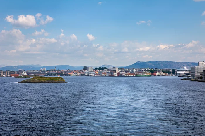 Blick auf eine Hafenstadt mit Bergen im Hintergrund und Wasser im Vordergrund unter blauem Himmel mit Wolken