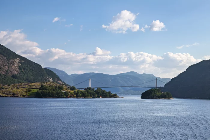 Brücke über einen ruhigen Fjord mit bewaldeten Bergen und blauem Himmel mit Wolken