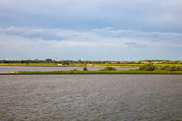 Flusslandschaft mit grünen Inseln und Windrädern am Horizont unter bewölktem Himmel