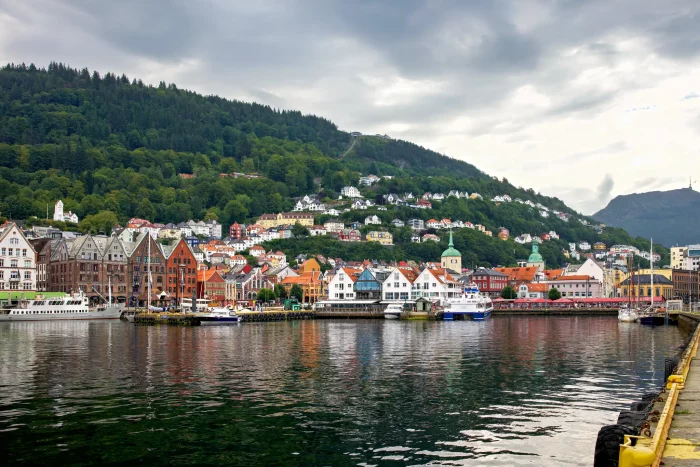 Blick auf den Hafen von Bergen mit bunten Holzhäusern am Wasser und bewaldeten Hügeln im Hintergrund