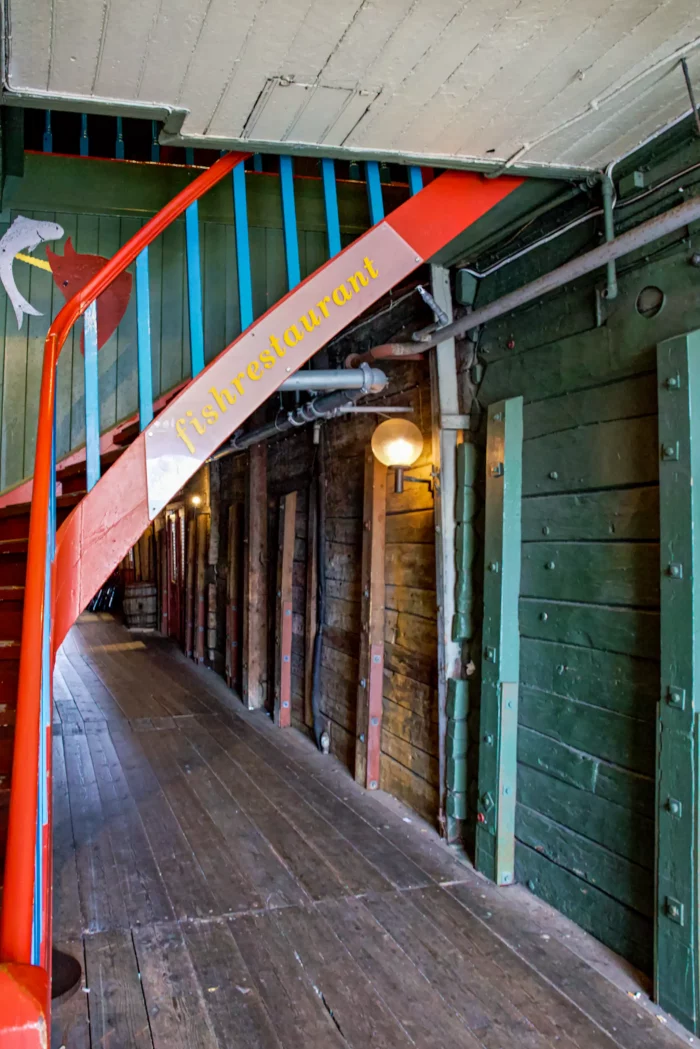 Holztreppe mit rotem Geländer und gelbem Schriftzug 'fishrestaurant' in einem historischen Lagerhaus mit grünen Holzwänden