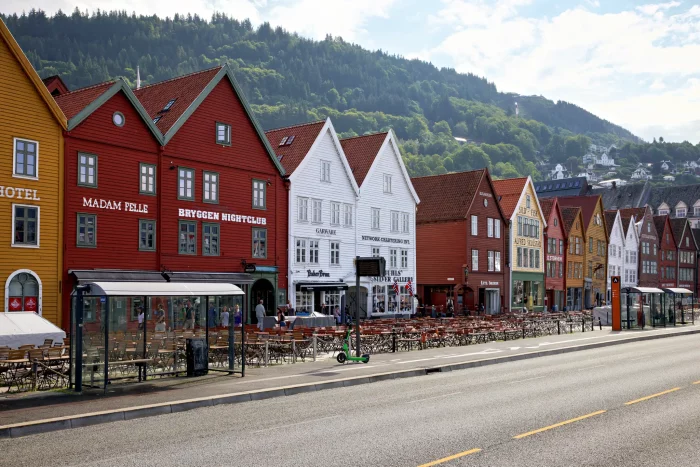 Reihe bunter Holzhäuser am Hafen von Bergen, Norwegen, vor bewaldeten Hügeln