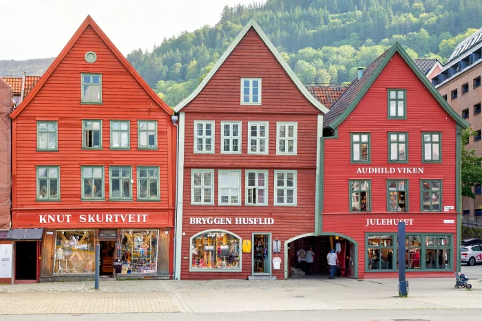 Drei rote Holzhäuser mit spitzen Dächern in Bergen, Norwegen, mit Geschäften Knut Skurtveit, Bryggen Husflid und Audhild Viken