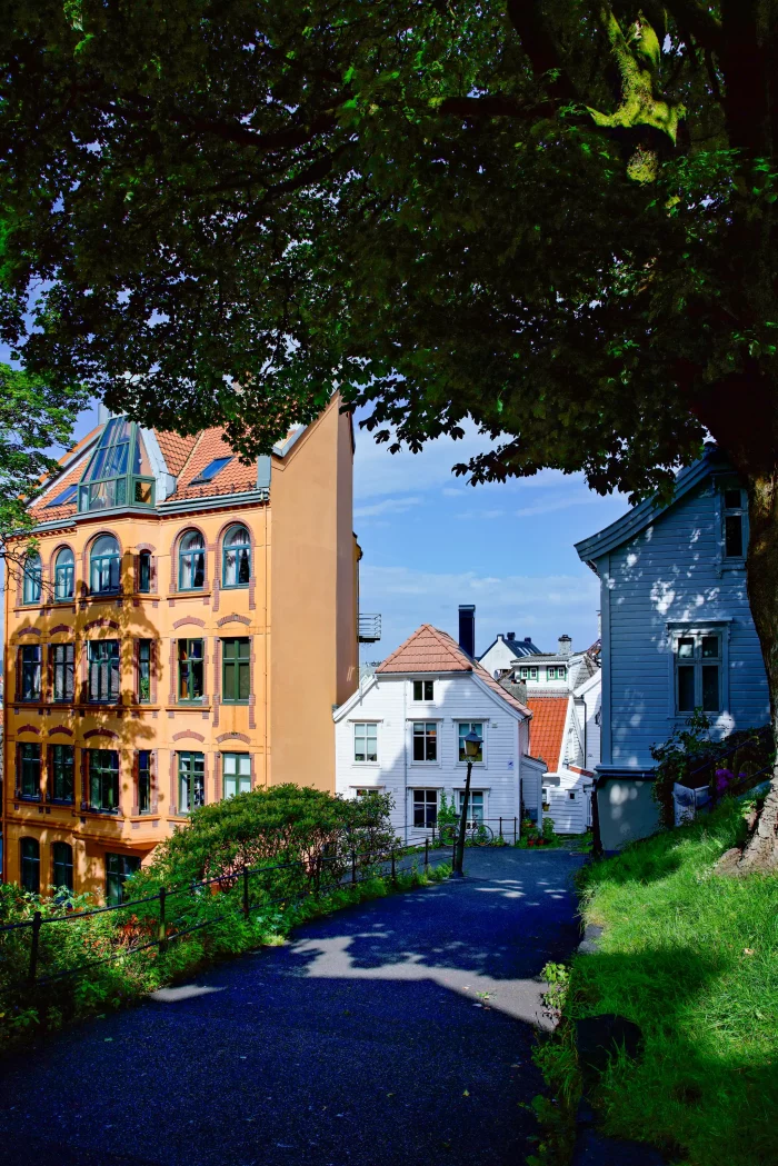 Weg zwischen grünen Bäumen führt zu bunten Häusern mit roten Dächern in einer Stadt