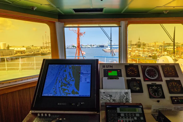 Blick vom Steuerstand eines Schiffes auf Hafen mit mehreren Schiffen und Hafenanlagen bei Sonnenuntergang
