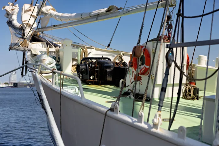 Vorderer Teil eines Segelschiffs mit Takelage, Seilen und Rettungsring am Deck bei klarem Himmel