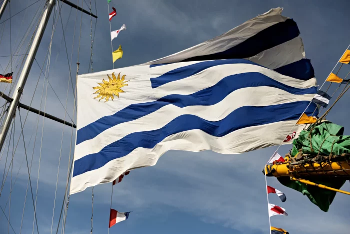Flagge von Uruguay mit Sonne und neun blauen und weißen Streifen weht an einem Mast bei klarem Himmel