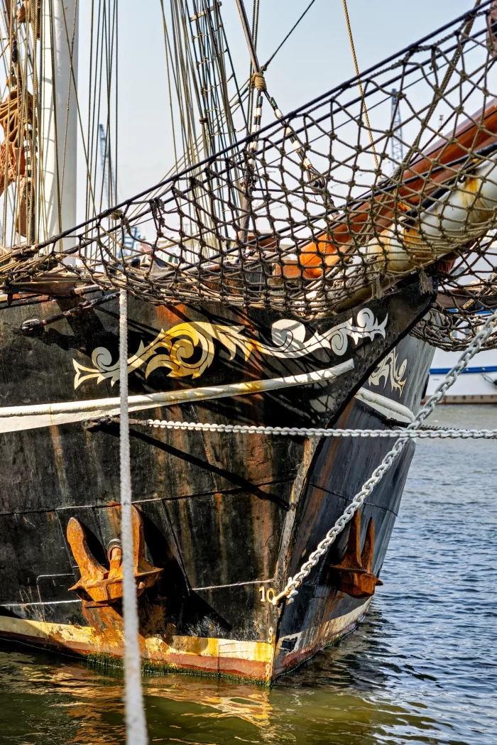 Bug eines historischen Segelschiffs mit verzierter Galionsfigur und Ankern im Hafen