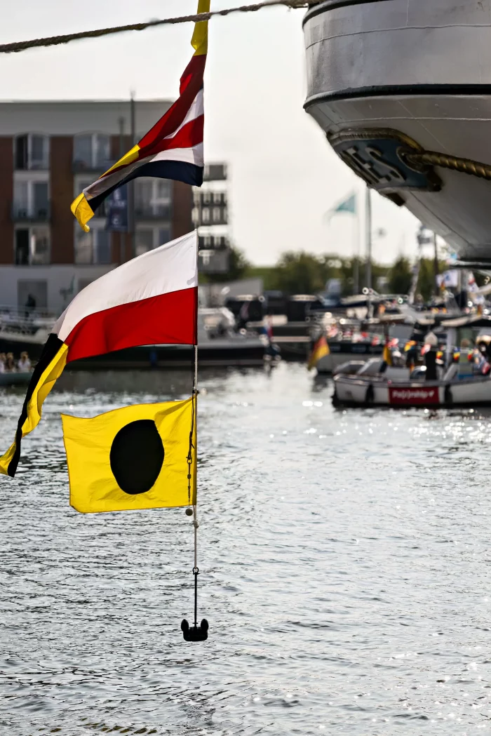 Mehrere maritime Signalfahnen an einem Schiff, im Hintergrund Boote und Gebäude am Wasser