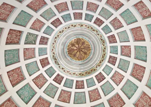 Blick nach oben auf die bemalte Kuppel im Englischen Garten München mit konzentrischen Ringen aus rot- und türkisfarbenen Quadraten und einem goldfarbenen Mittelkreis mit floralem Muster.