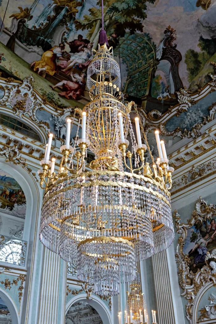 Großer Kronleuchter mit Kerzen und Kristallanhängern in prunkvollem Raum mit bemalter Decke im Schloss Nymphenburg, München.
