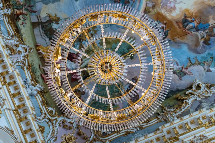 Goldene Kronleuchter mit Kristallanhängern an bemalter Decke im Schloss Nymphenburg in München.