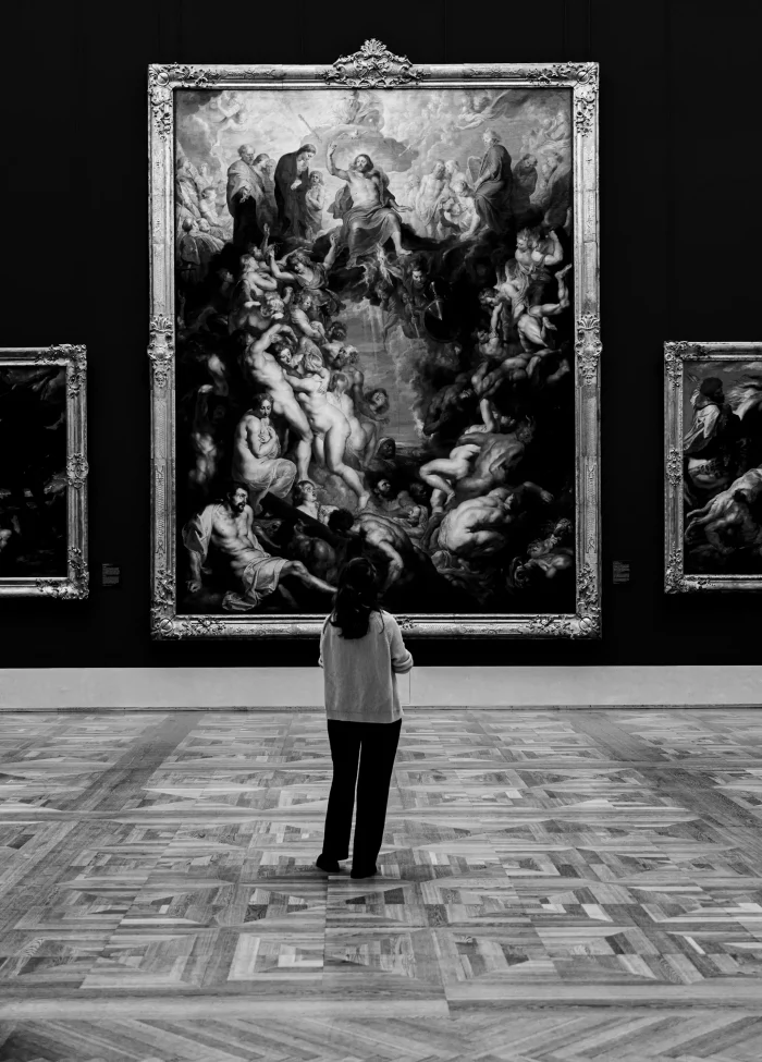 Person von hinten vor großem, barockem Gemälde mit zahlreichen Figuren in Museumssaal mit Parkettboden