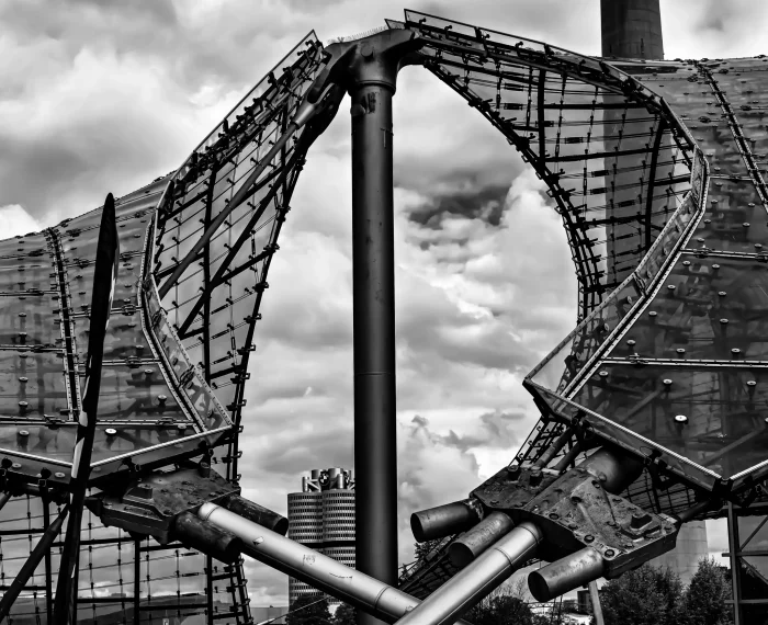 Schwarz-weiße Nahaufnahme der Stahl-Glas-Konstruktion des Olympiastadions München mit dem BMW-Vierzylinder-Hochhaus im Hintergrund.