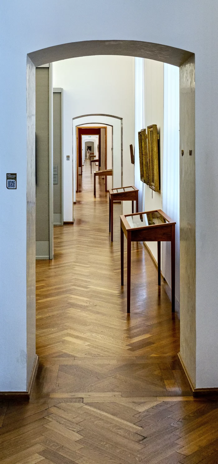 Blick durch mehrere Türöffnungen in einem Museumsgang mit Holzböden, weißen Wänden und Vitrinen sowie Gemälden an der rechten Wand.