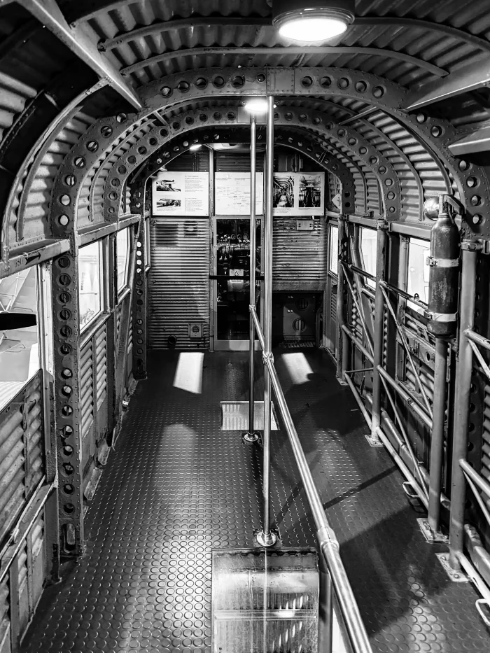 Innenraum eines historischen Flugzeuges mit gewölbter Decke, Metallstreben und Haltestangen in der Mitte.