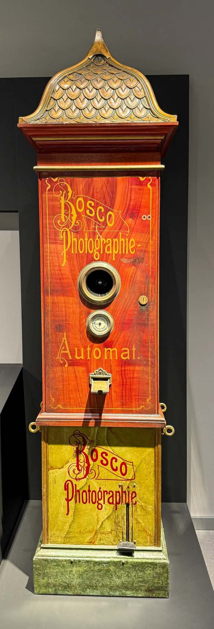 Holzgehäuse einer historischen Fotokabine mit der Aufschrift 'Bosco Photographie Automat', zwei runden Objektiven und einem Münzschlitz.