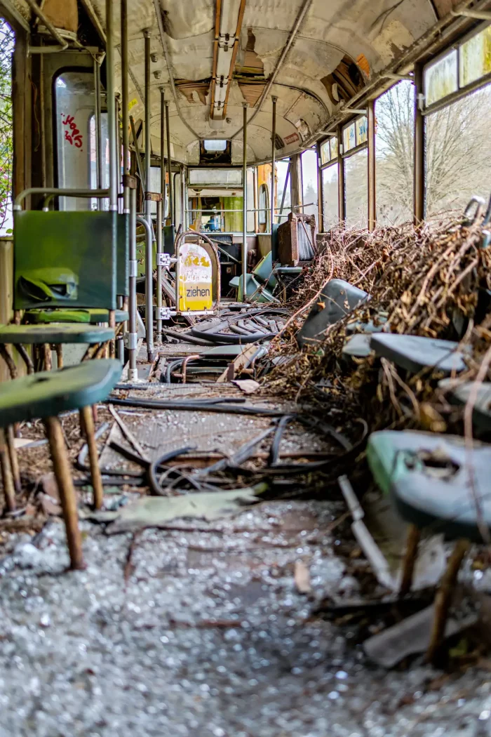 Innenraum eines verfallenen Straßenbahnwagens mit zerstörten Sitzen, herumliegenden Ästen und Schutt auf dem Boden