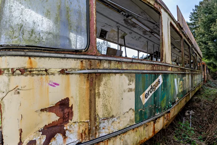 Verfallene Straßenbahn mit abgeblättertem Lack, Roststellen und verblasster Werbung in einer bewachsenen Umgebung