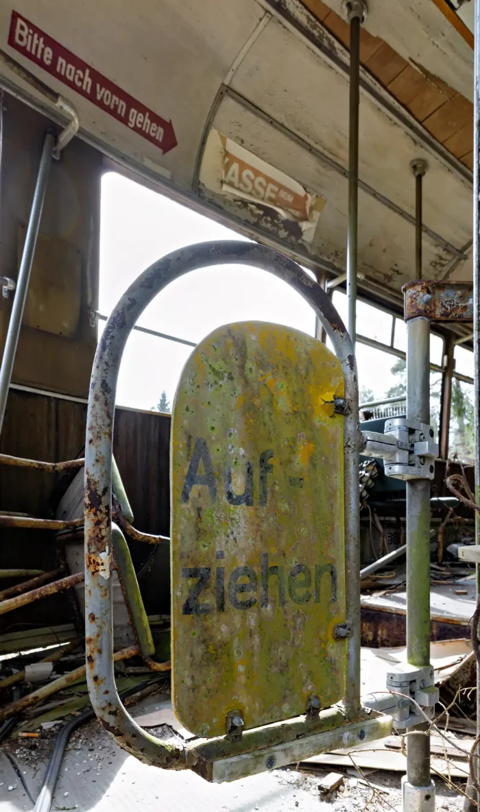 Verrosteter gelber Schild mit der Aufschrift 'Aufziehen' in einer verfallenen Straßenbahn mit sichtbaren Metallstreben und zerbrochenen Fenstern.