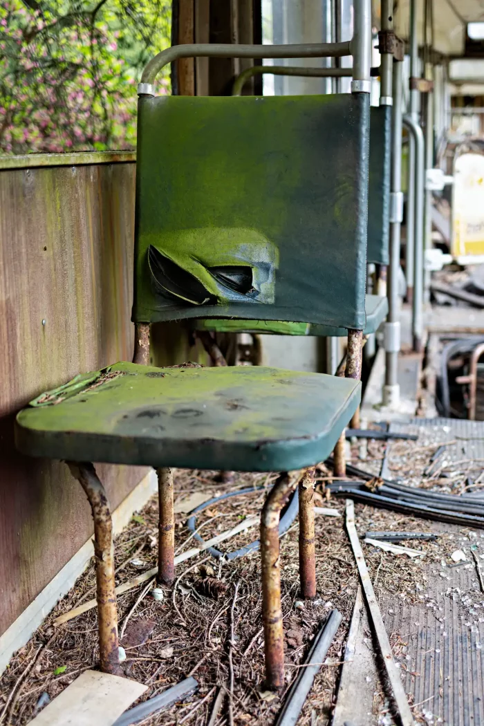 Verrosteter Metallstuhl mit zerrissenem, moosbedecktem Sitz und Rückenlehne in einer verfallenen Straßenbahn