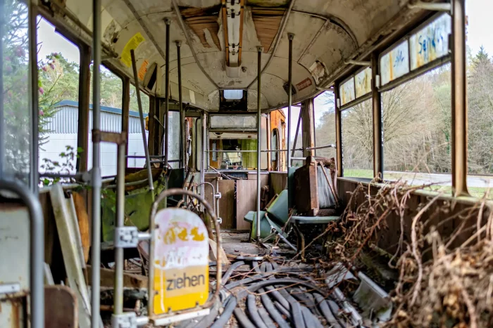 Innenraum einer verfallenen Straßenbahn mit zerstörten Sitzen, freiliegenden Kabeln und überwucherten Pflanzen an den Fenstern
