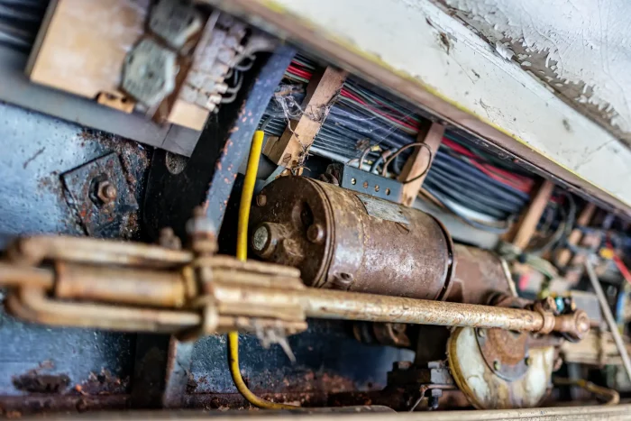 Nahaufnahme eines verrosteten mechanischen Teils mit Kabeln in einer alten verfallenen Straßenbahn