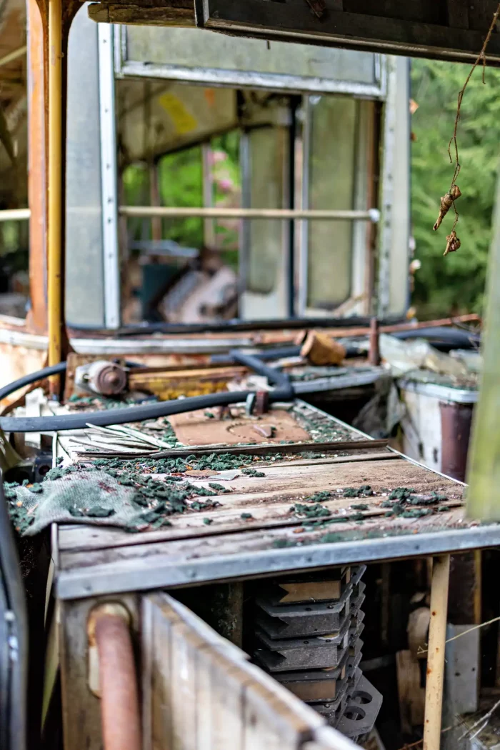 Innenansicht einer verfallenen Straßenbahn mit verrosteten Metallteilen, zerbrochenen Fenstern und überwuchertem Bedienpult