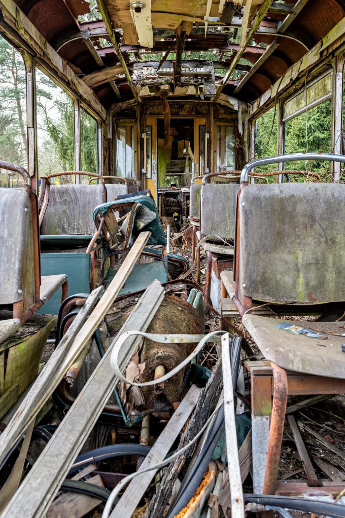 Innenraum einer verfallenen Straßenbahn mit zerstörten Sitzen, rostigen Metallteilen und Trümmern auf dem Boden, umgeben von Wald