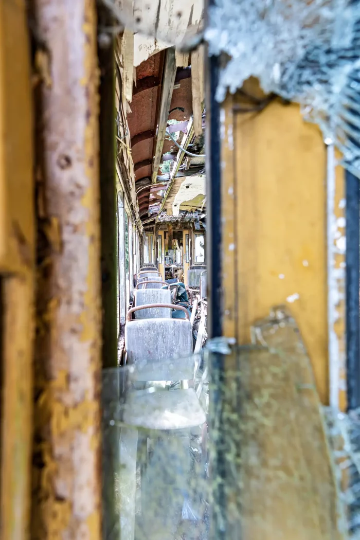 Blick durch einen schmalen Spalt auf die verfallene Innenausstattung einer alten Straßenbahn mit beschädigten Sitzen und rostigen Metallteilen